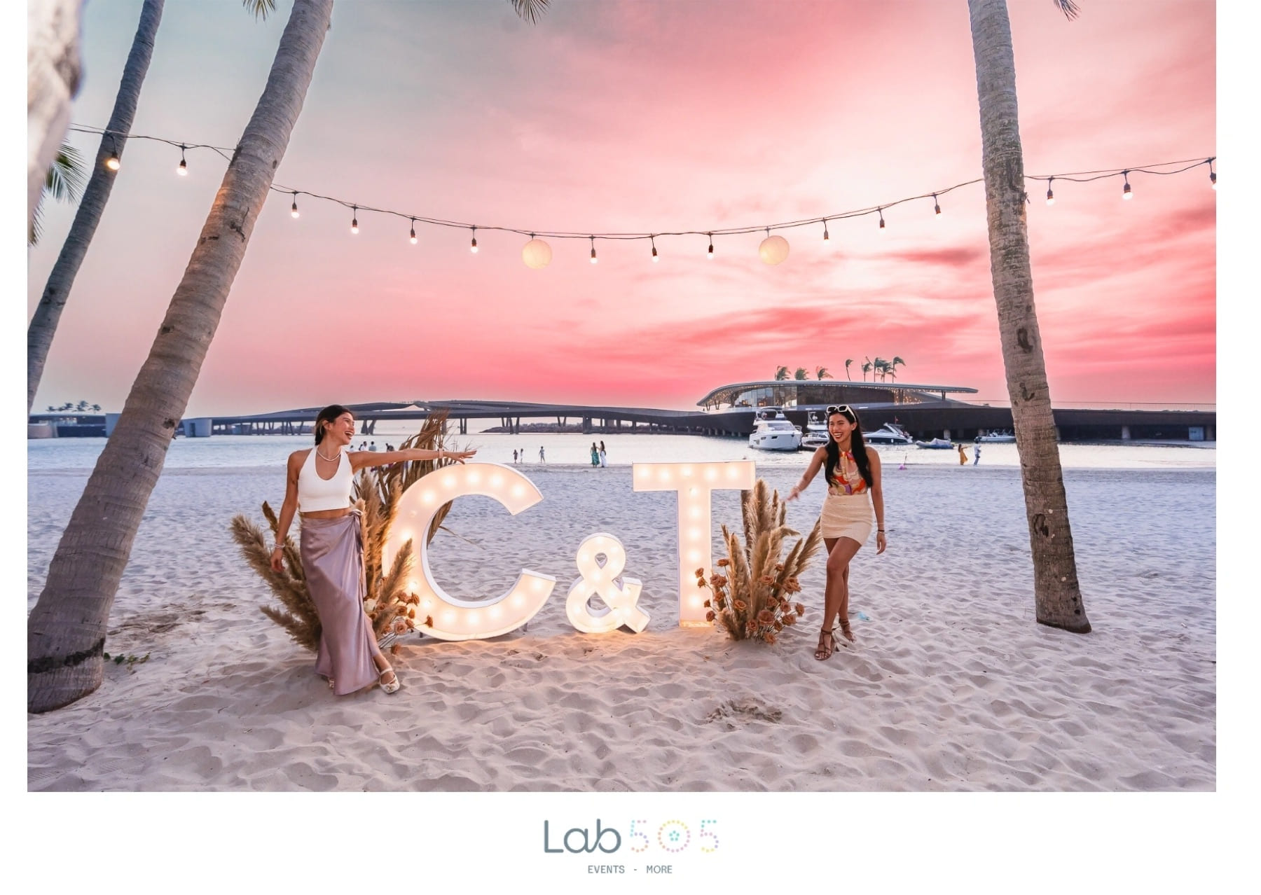 C and T illuminated letters beneath palms at a pink beach sunset