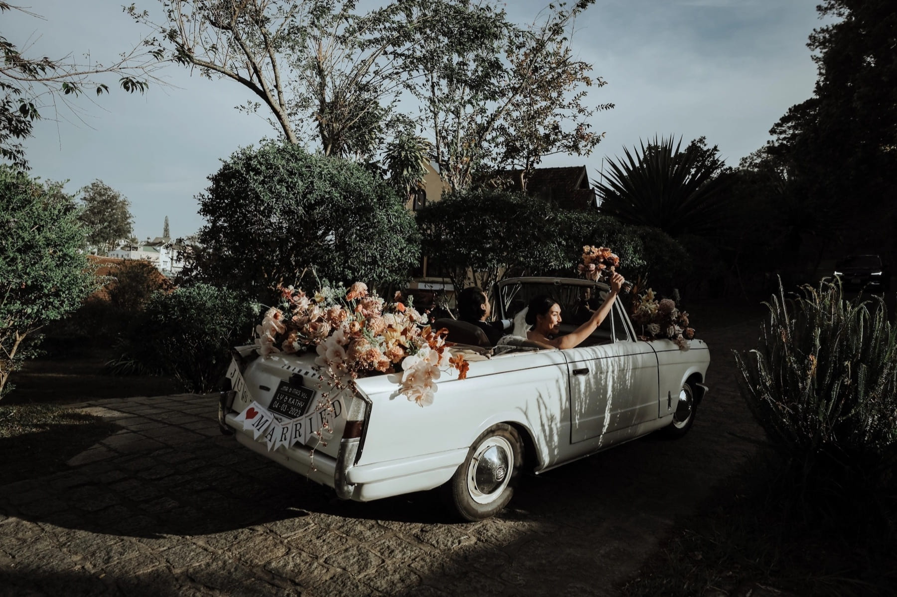 Couple leaving their woodland celebration in a flower-covered vintage car