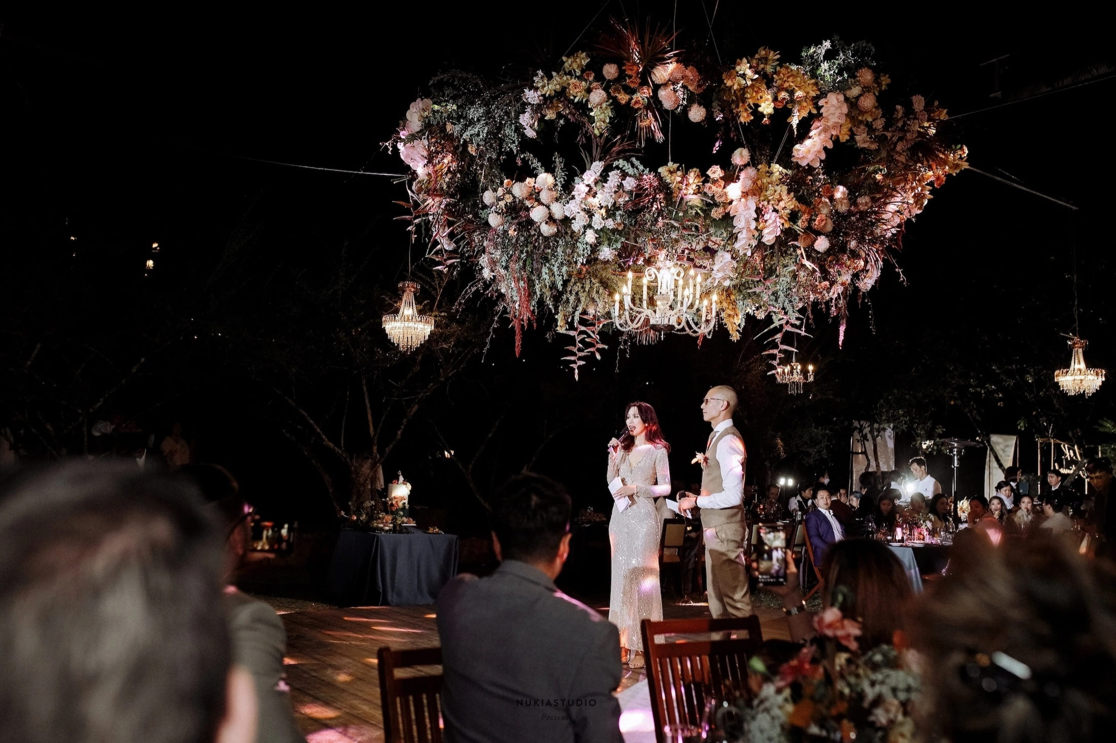 An evening celebration staged beneath flowers and chandeliers